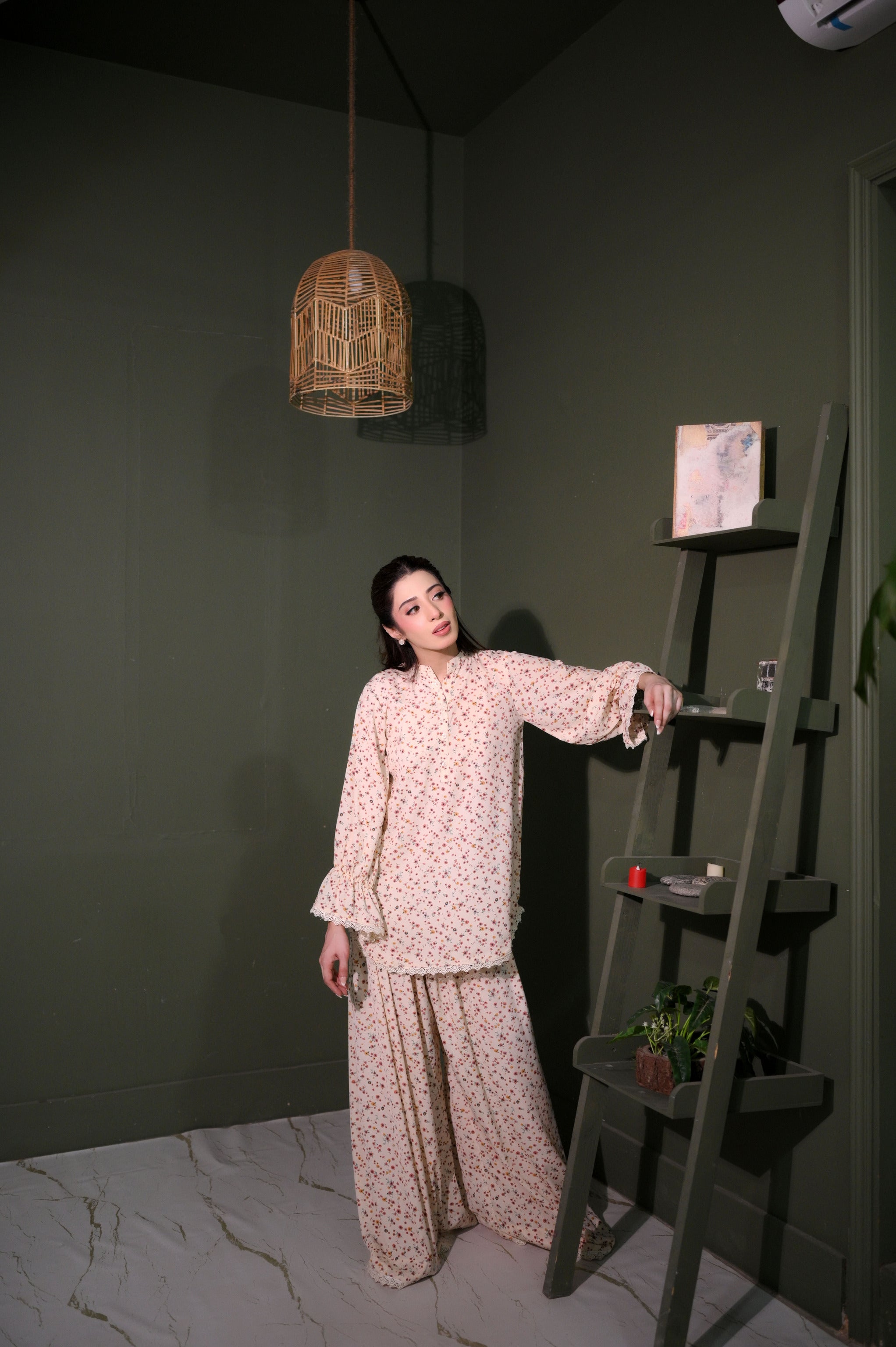 Woman in a floral outfit standing next to a ladder against a dark wall.